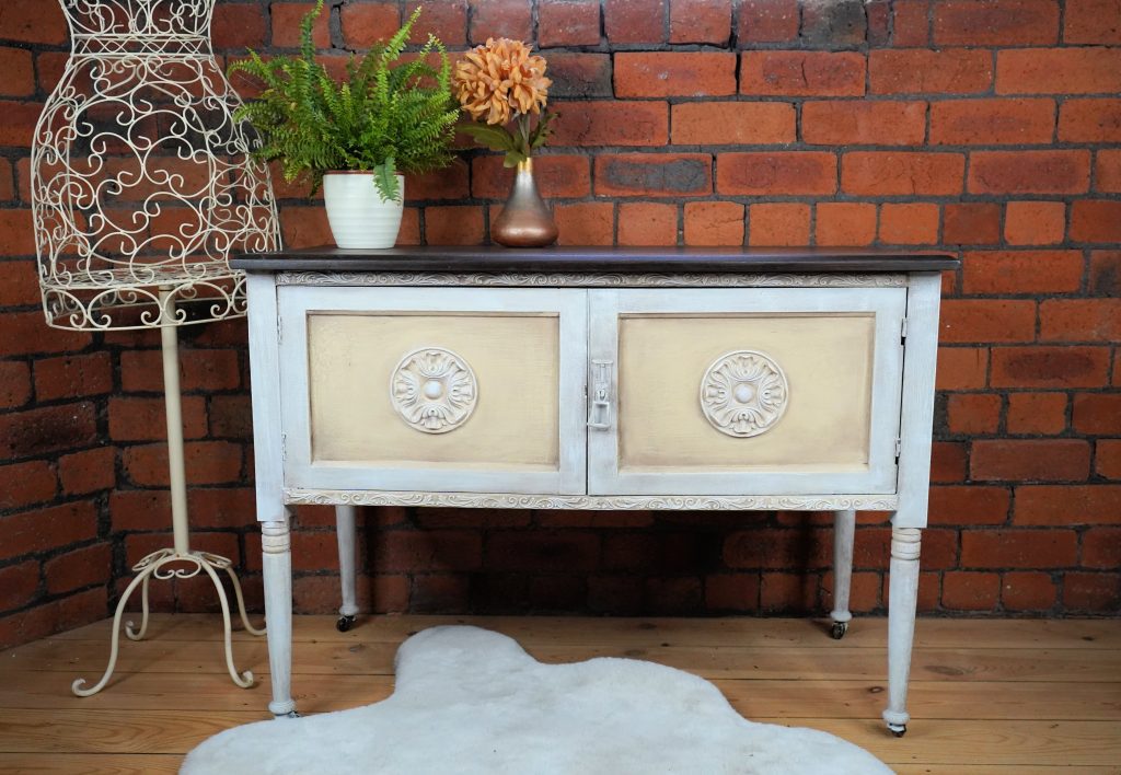 A picture of a Shabby Chic painted Blanket Box with a white wash and pale yellow inserts. WoodUBend Moldings added to the door fronts to give character. Staged with floral bouquet, house plant and dress mold.