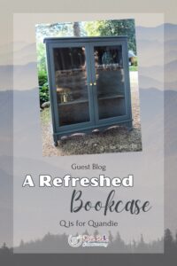 A tall gray painted cabinet with glass doors that have gold knobs sitting on a dirt ground with trees and greenery in the background is above of the words Guest Blog Refreshed Bookcase Q is for Quandie. The background is the Great Smoky Mountains.