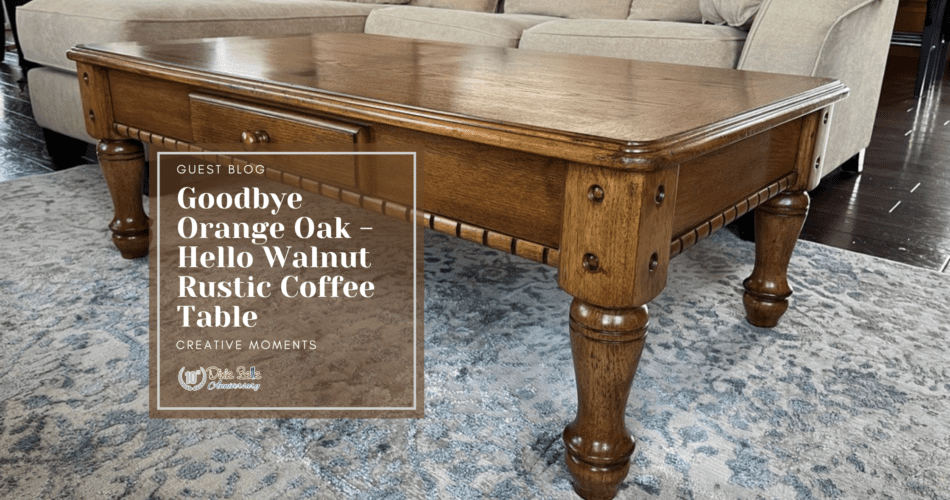 A brown wooden coffee table sitting on a blue and gray rug. A green plant sits on top of the table in a black pot. A tan sofa with a white blanket draped over it is behind the table. In front of the table is a brown box with the words Guest Blog, Goodbye Orange Oak - Hello Walnut Rustic Coffee Table Creative Moments printed in white.