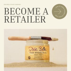 A photo of an open jar of Dixie Belle Chalk Mineral Paint in Sand Bar sitting on a table covered with sand. A paint brush with paint on it is lying across the top of the paint jar. Above the jar are the words Become A Retailer.