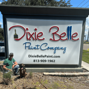 Kevin Fulford and Huck sitting on the ground next to the Dixie Belle Paint Company sign