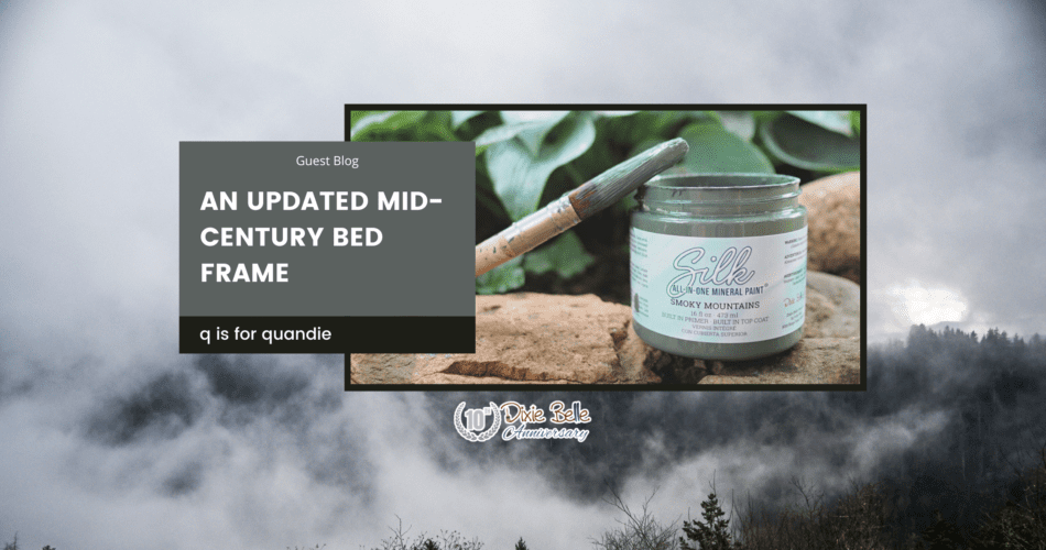 An open jar of Smoky Mountains Silk All-In-One Mineral Paint sitting on a brown rock with greenery in the background. A paint brush with paint on the bristles sits across the top of the jar. The words "an updated mid-century bed frame" are printed to the left of the paint jar. The entire background of the picture is a photo of the Great Smoky Mountains.