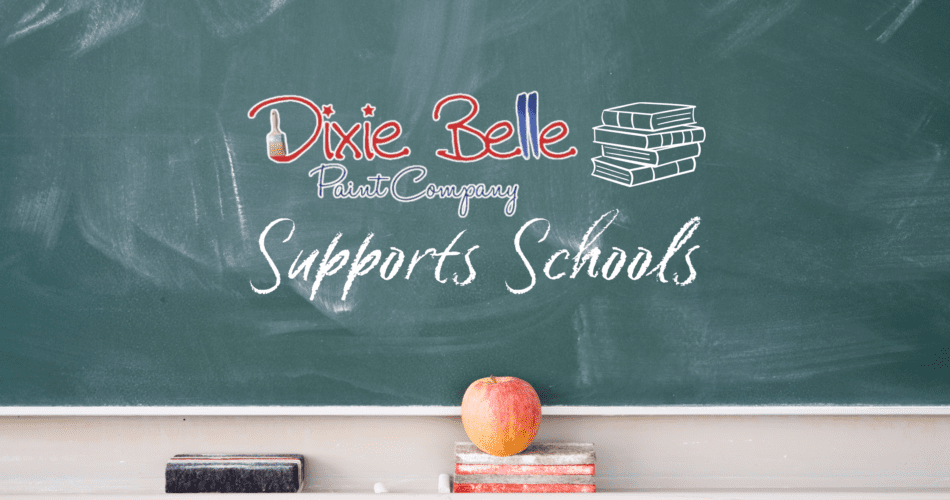 A green chalk board with Dixie Belle Paint Company logo, Supports Schools and a stack of 4 books on the chalk board. The tray below the chalkboard holds a black eraser, a red eraser and a red apple.