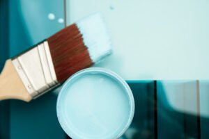 an open jar of Dixie Belle Blue Chalk Mineral Paint with a paint brush with paint on the bristles sitting next to the jar of paint. All are on a blue background.