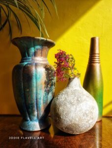 3 painted vases sitting on a brown tabletop in front of a yellow painted wall