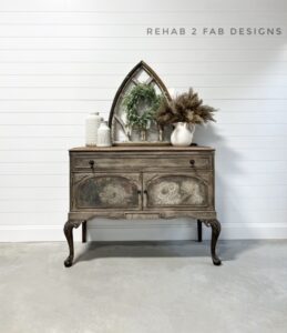 A photo of a brown painted buffet sitting on a white floor, in front of a white wall