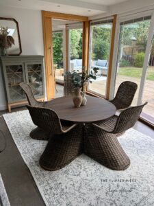 a photo of a brown painted wooden table and brown painted wicker chairs sitting on a white rug in front of white painted sliding glass doors