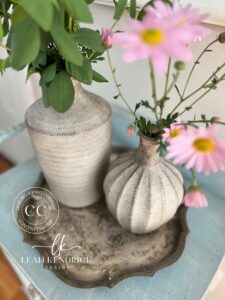 two painted vases with greenery coming out of them sitting on a brown tray on top of a blue table