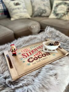 A brown painted tray with the Snowed In decoupage paper applied tot he top of it with a small figurine of Santa and a small white sleigh with pine cones in it.