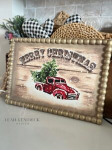 A gold and brown painted tray with the Snowed In decoupage paper applied to the front of it sitting on a white countertop