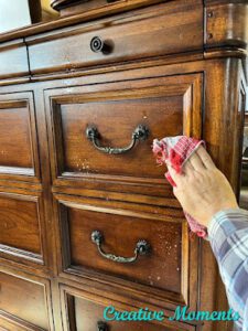 A hand cleaning the brown wooden dresser using a white and red cloth.