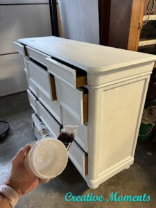 A dresser that has been painted with Bonding BOSS; a hand holds a paint brush and an empty jar of Bonding BOSS in front of the dresser.