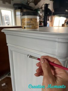 A nightstand that has been painted with Bonding BOSS that has a jar of Bonding BOSS sitting on top of it. A hand holds an artist brush in front of the nightstand.