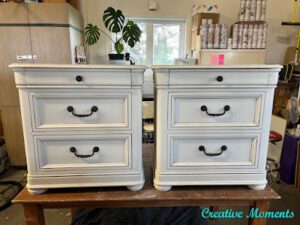 A pair of white painted nightstands sit on top of a brown wooden table