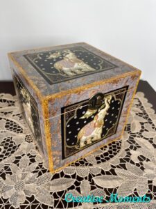 "Before" picture of painted wooden box sitting on a brown wooden table on a white lace doily; the box has a white and pink elephant painted on all sides