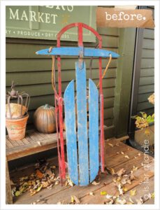 A blue and red faded wooden sled standing up on a brown wooden floor, in front of a green wall