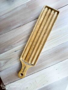 A rectangular wooden breadboard with a handle sitting on a wooden table